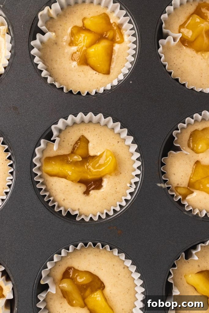 batter for apple pie cupcakes prepared in muffin tin with dollops of pie filling in the center