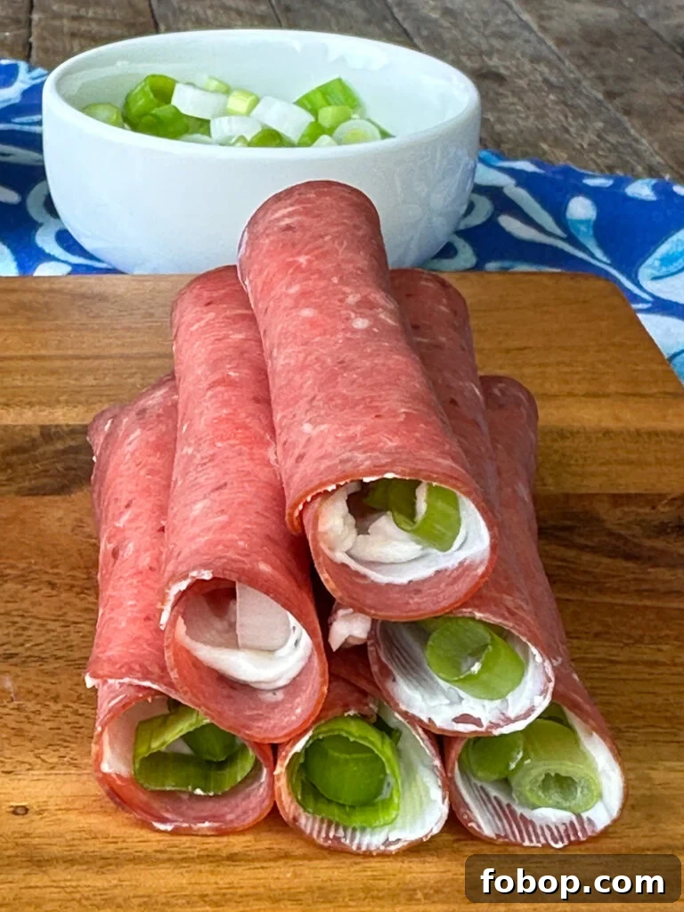 Savory Dried Beef Roll-Ups Recipe for Appetizers and Snacks 12 Close up pyramid of dried beef roll-ups with slices of green onions in the center on a wooden board.