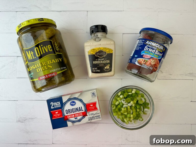 Savory Dried Beef Roll-Ups Recipe for Appetizers and Snacks 4 Ingredients to make dried beef roll ups are kosher baby dill pickles, creamy horseradish, armour dried beef, cream cheese and sliced green onions on a white counter top.
