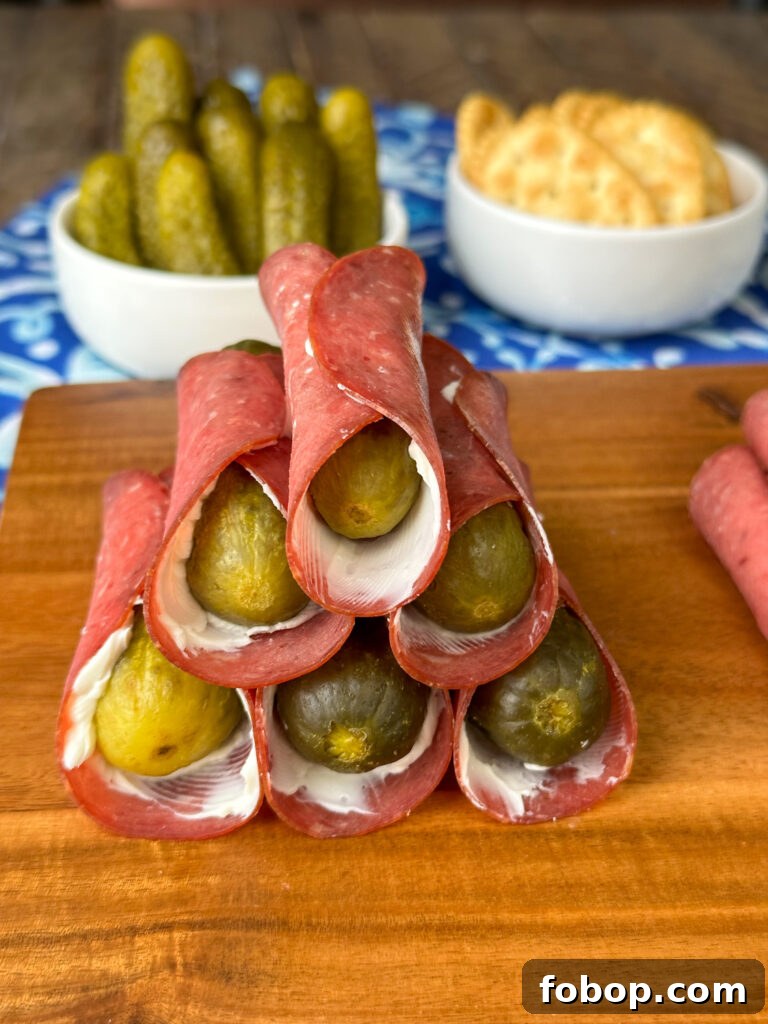 Savory Dried Beef Roll-Ups Recipe for Appetizers and Snacks 10 Stack of pickle roll-ups with dried beef and cream cheese on a wooden cutting board with more baby dill pickles in the background.