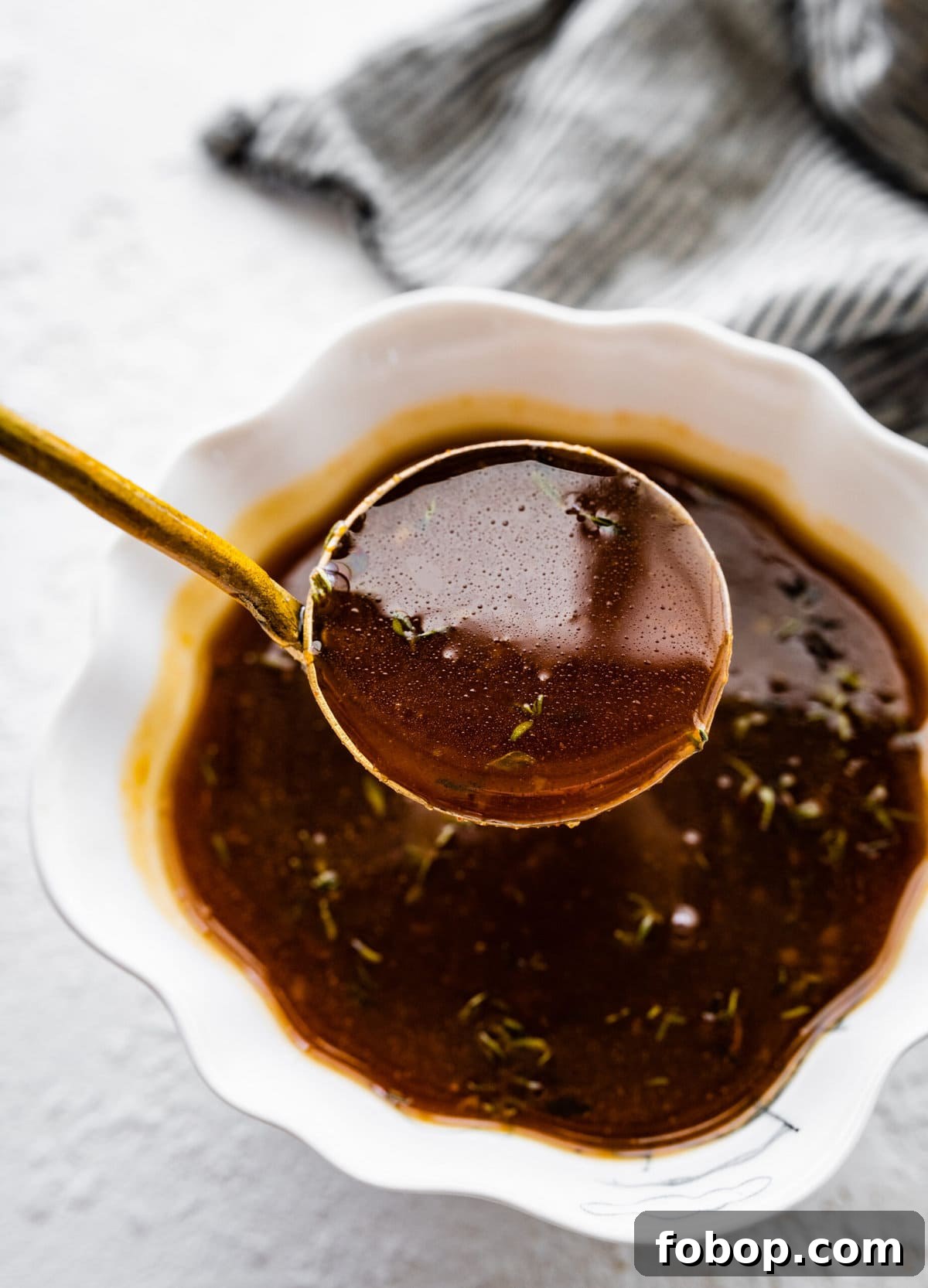 Brown sugar glaze for ham in a bowl with a ladle lifting a portion up.