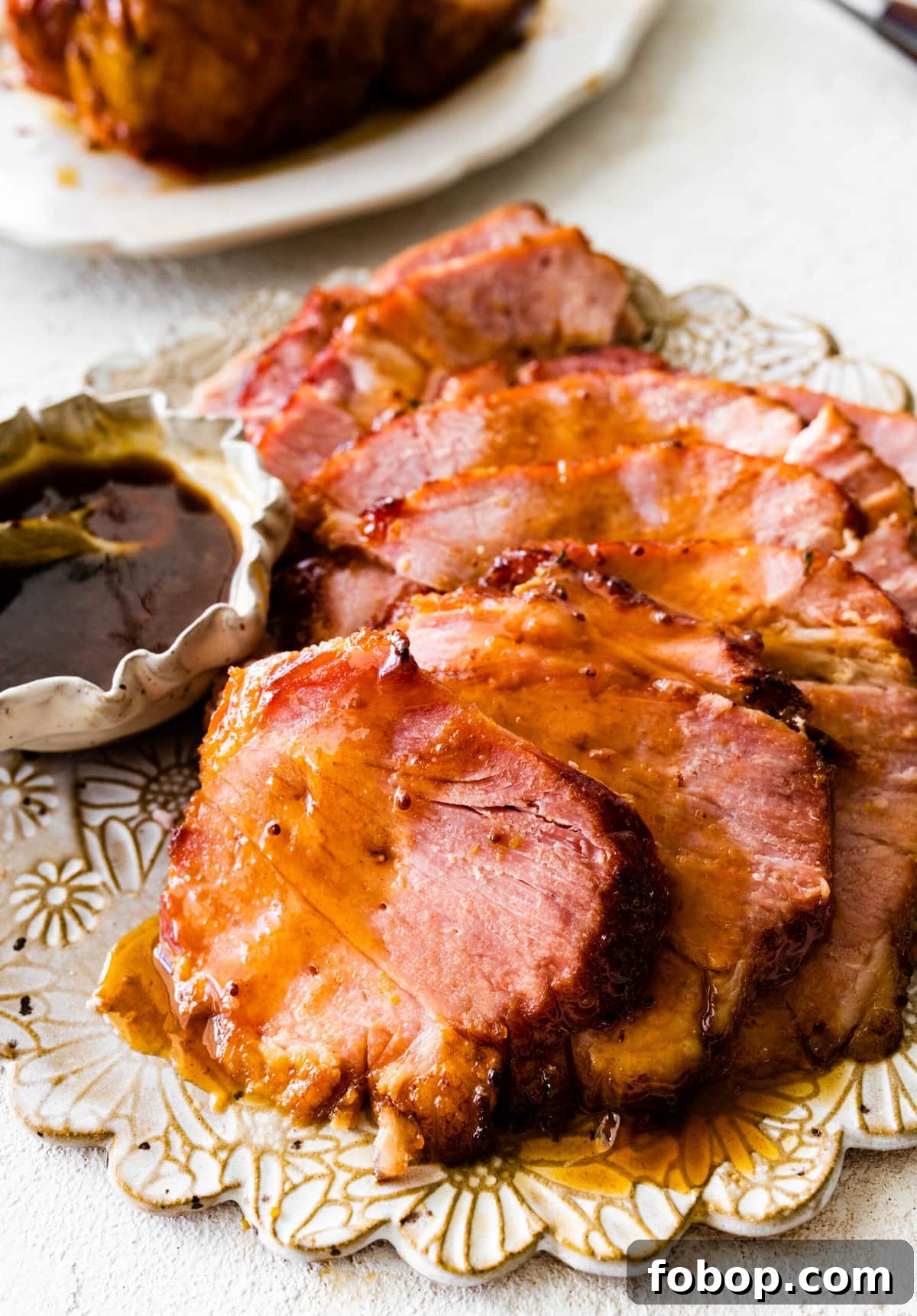 Slices of baked ham on a serving platter with brown sugar glaze on the side.