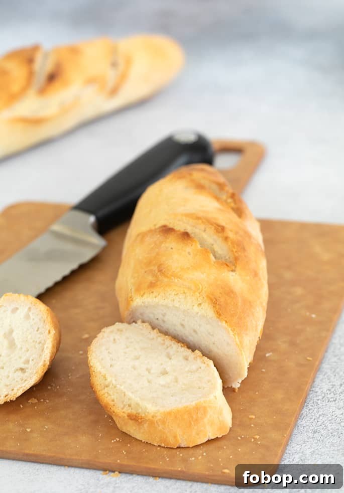 Crispy Gluten-Free French Baguettes: Artisan-Style Recipe 7 Two loaves of light brown baguette shaped bread, one partially sliced with bread knife on light brown cutting board