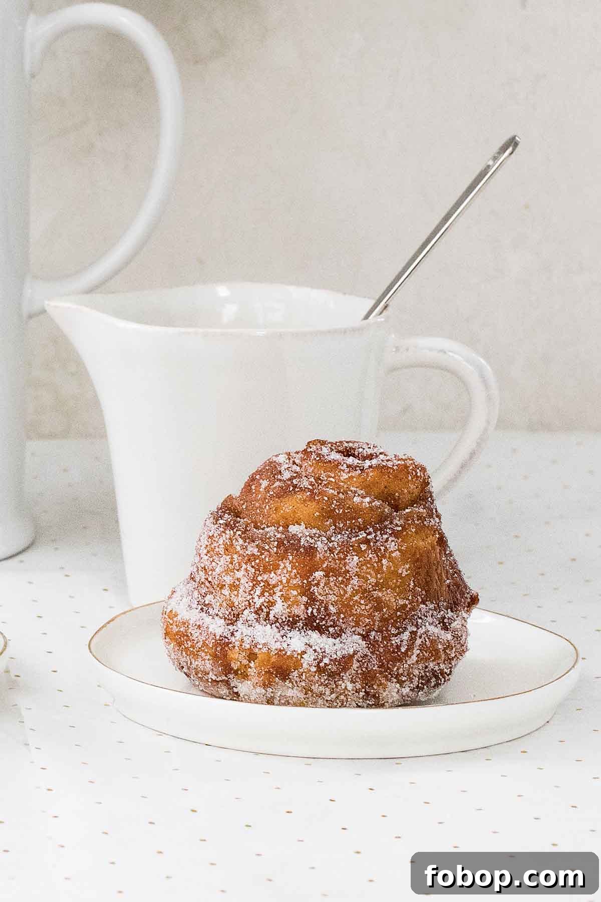 Perfectly Flaky Morning Buns: Cinnamon Sugar Pastry Recipe 4 A single golden-brown morning bun with flaky layers sitting on a small white plate.