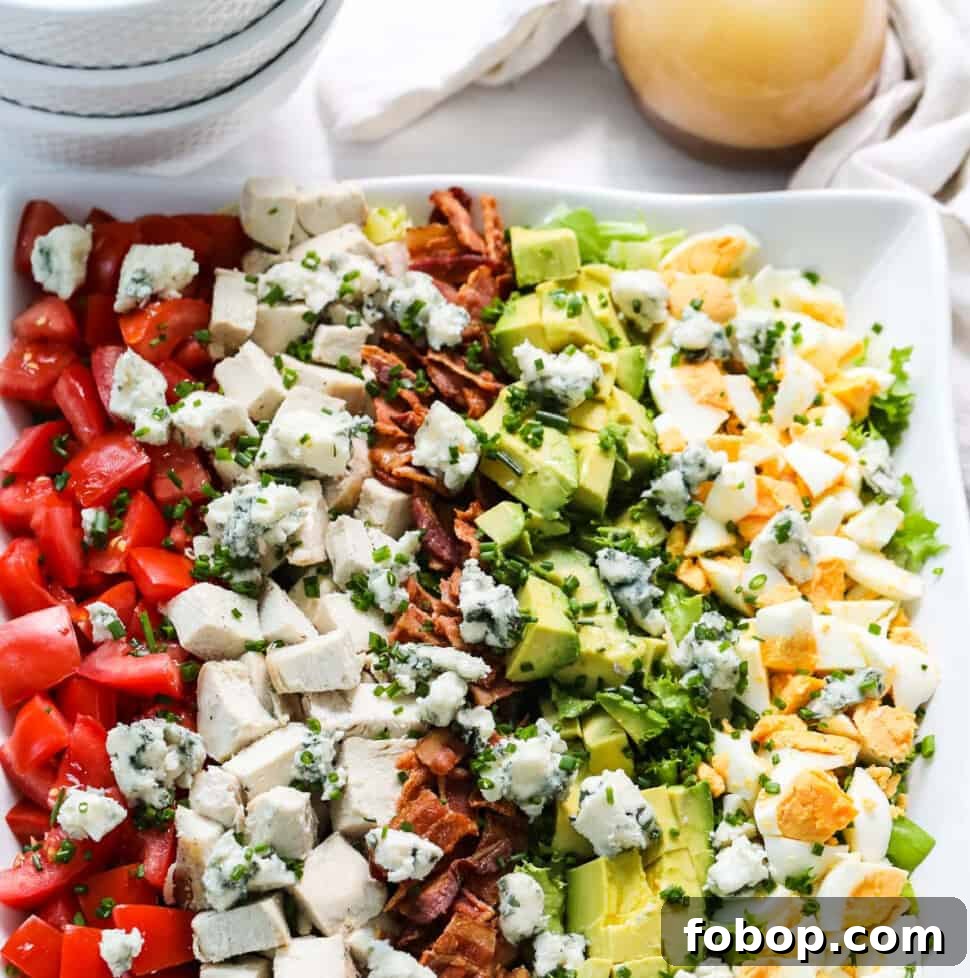 Classic Cobb Salad Recipe with Homemade Dressing and Tips 12 A white square plate filled with colorful Cobb Salad made with chicken, eggs, avocados, tomatoes, and bacon.