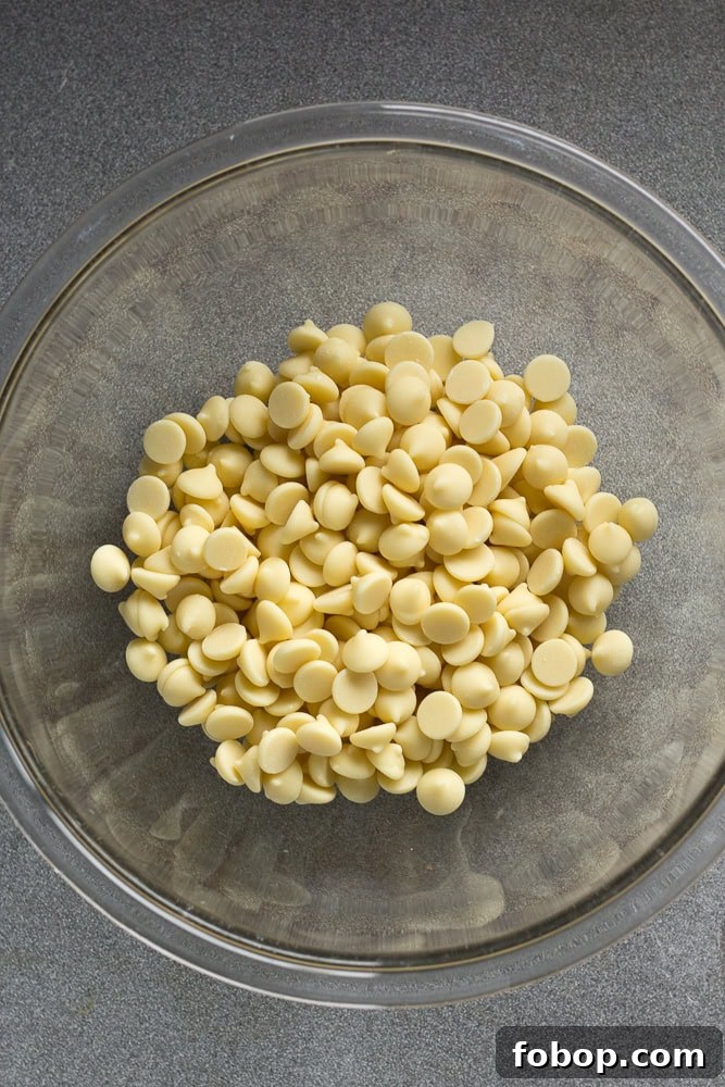 Gluten-Free White Chocolate Peppermint Bark Recipe 4 A clear bowl with white chocolate chips in it on a gray background.