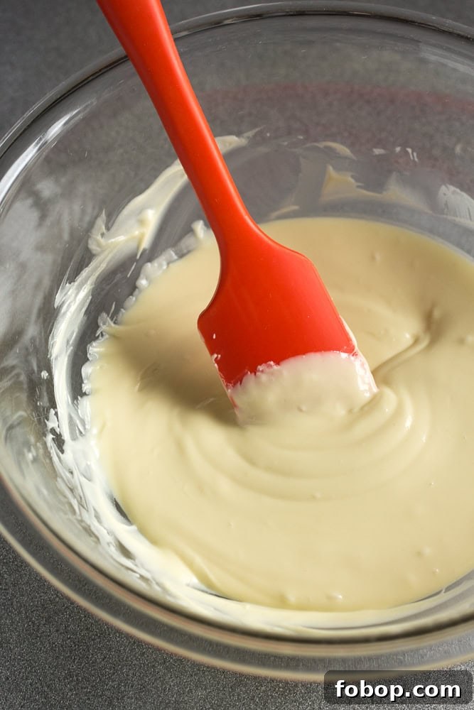 Gluten-Free White Chocolate Peppermint Bark Recipe 6 Melted white chocolate in a bowl with a red spatula.