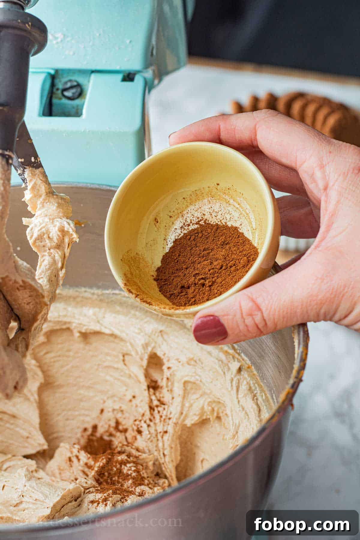 White Chocolate Biscoff Cookie Recipe: Crunchy Layered Cookies 6 Small yellow bowl of cinnamon pouring into bowl of raw cookie dough.