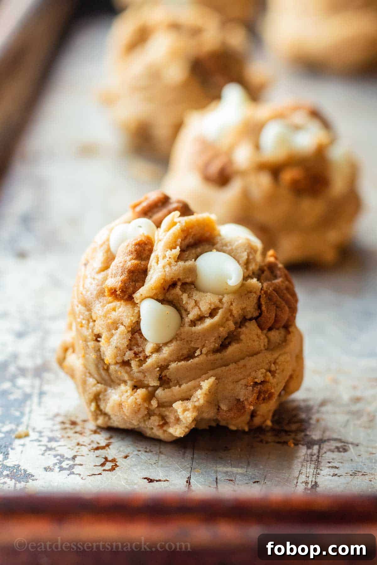 White Chocolate Biscoff Cookie Recipe: Crunchy Layered Cookies 8 Close up shot of raw cookie dough ball on metal baking sheet.