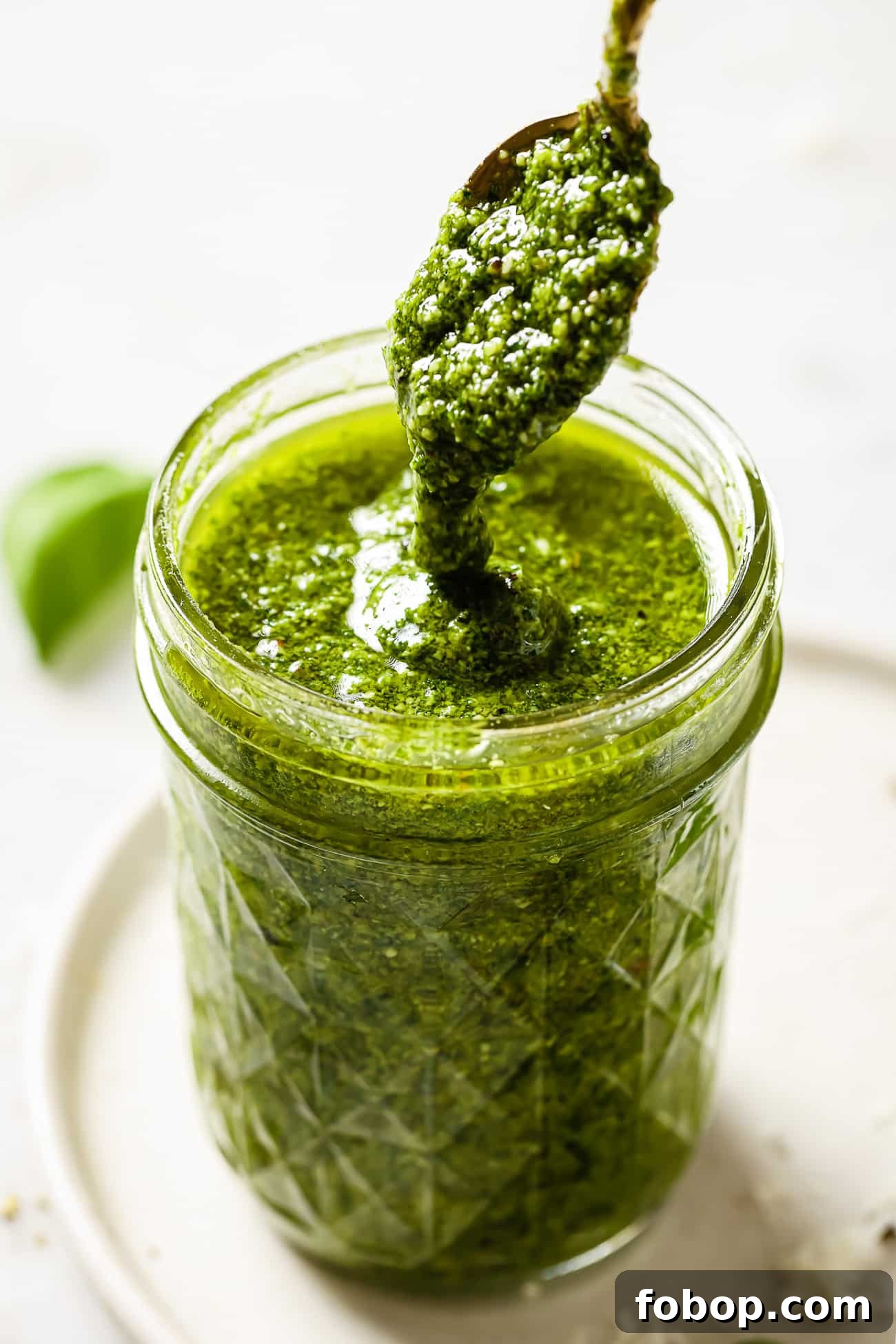 A spoonful of pesto being drizzled into a jar of pesto.