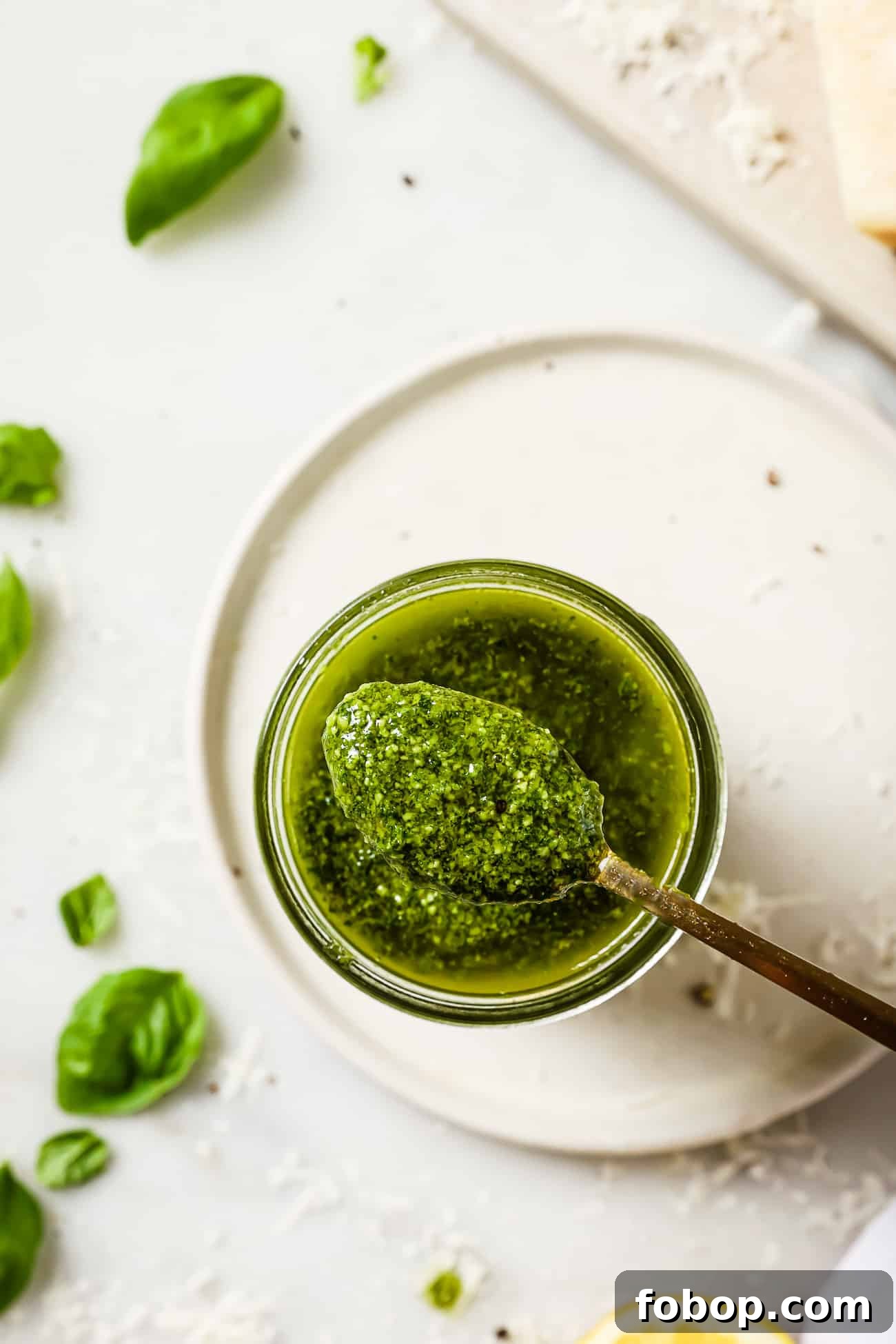 A spoonful of basil pesto resting on a jar of pesto.