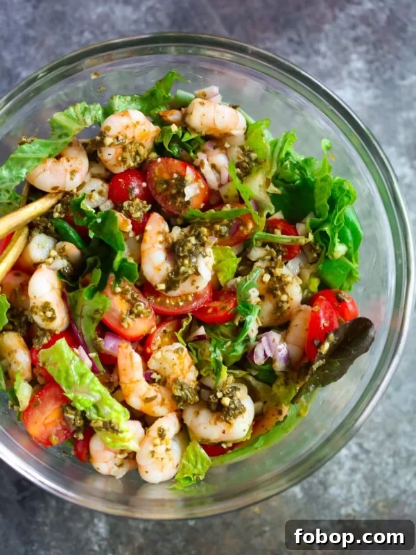 Glass bowl containing pesto shrimp tomato salad.