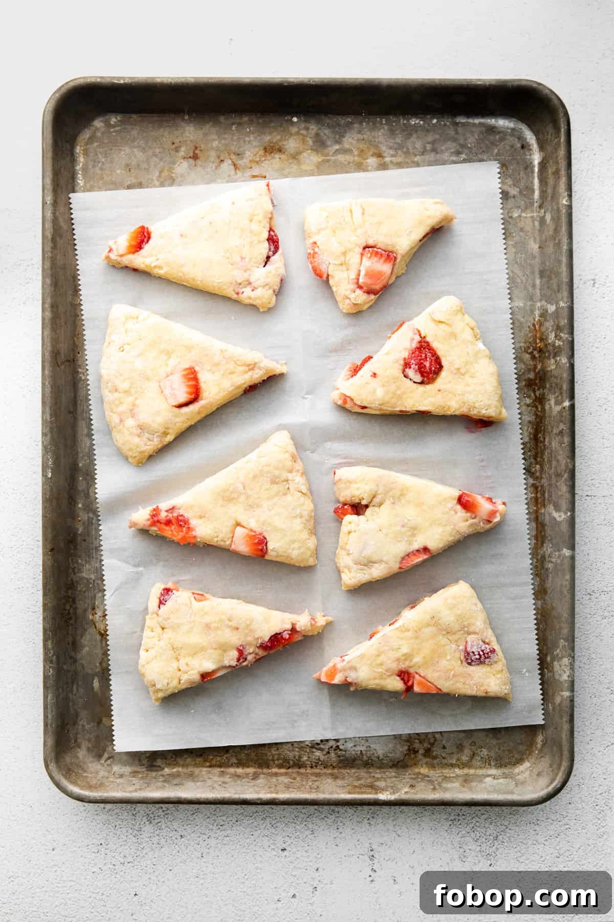 eight unbaked strawberry scones cut into triangles and placed on a parchment-lined baking sheet