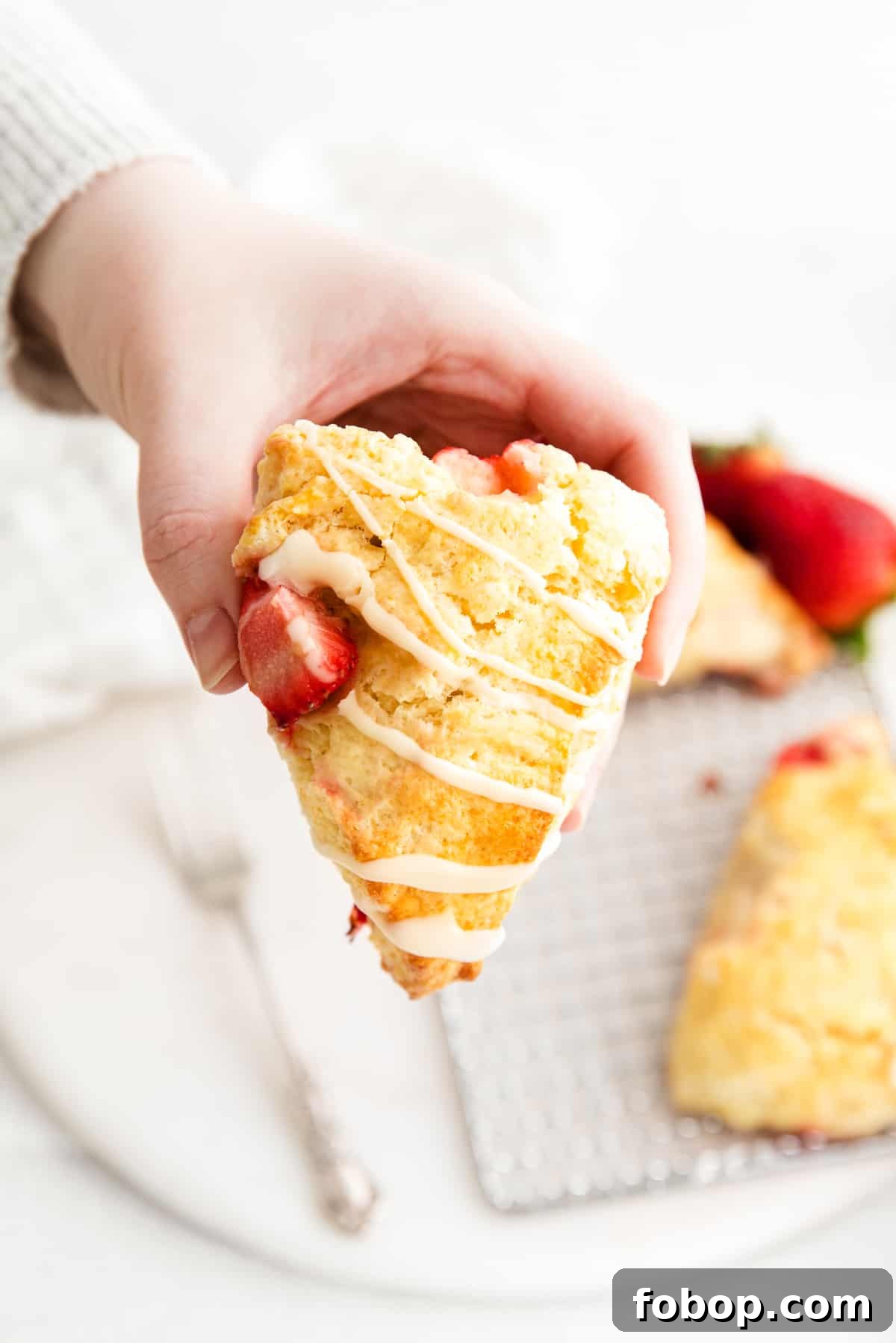 hand holding strawberry scone with additional scone in background