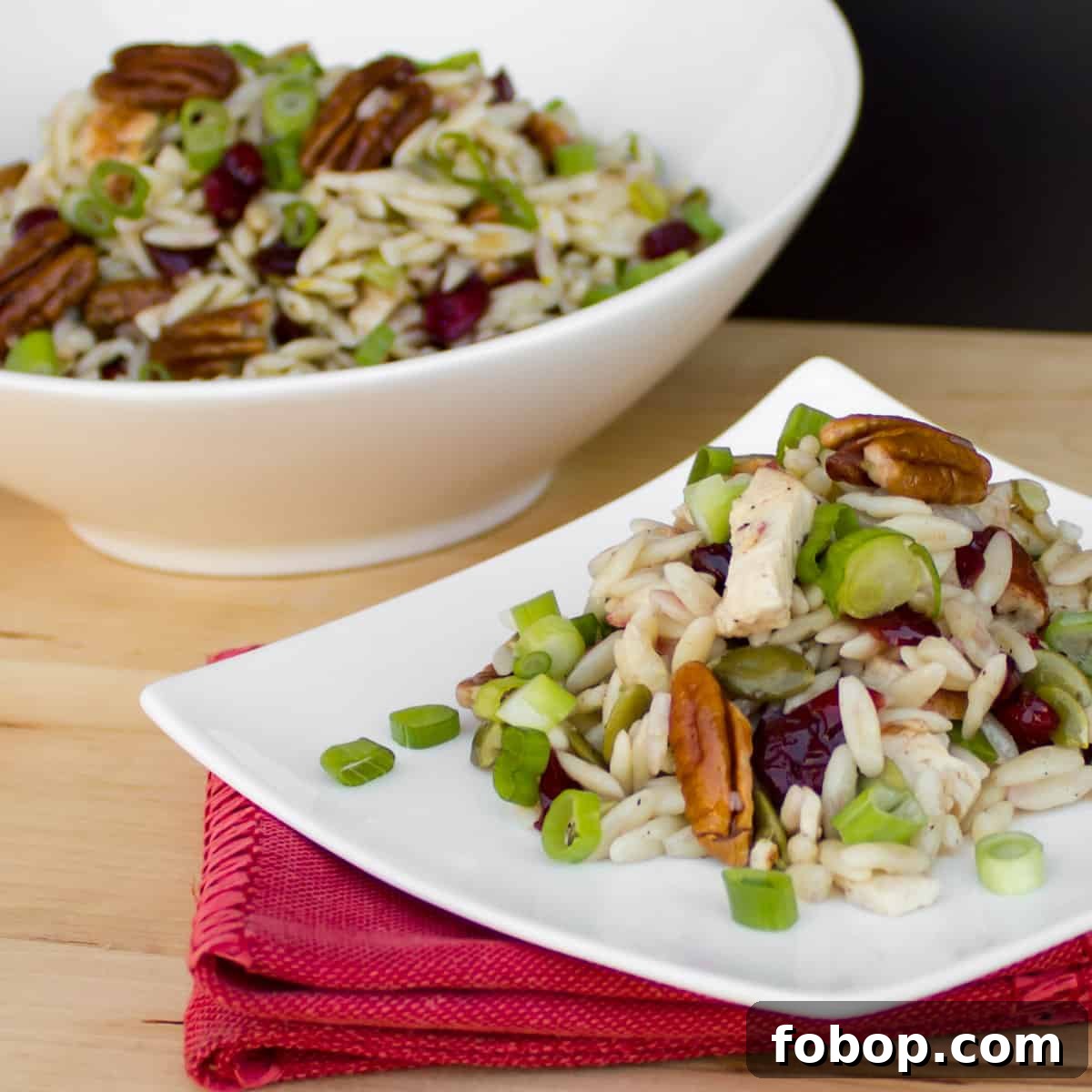 Pasta salad on a white plate in front of a full bowl of salad.
