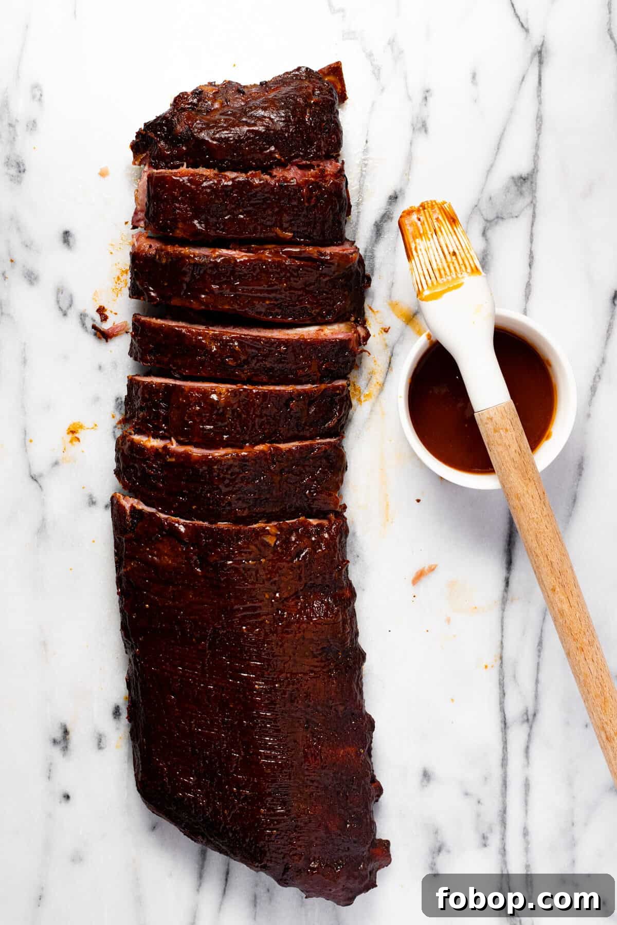 Smoked Baby Back Ribs: Tender, Flavorful Recipe for Beginners 10 White marble counter top with a rack of ribs, half of them sliced, and a bowl of BBQ sauce.