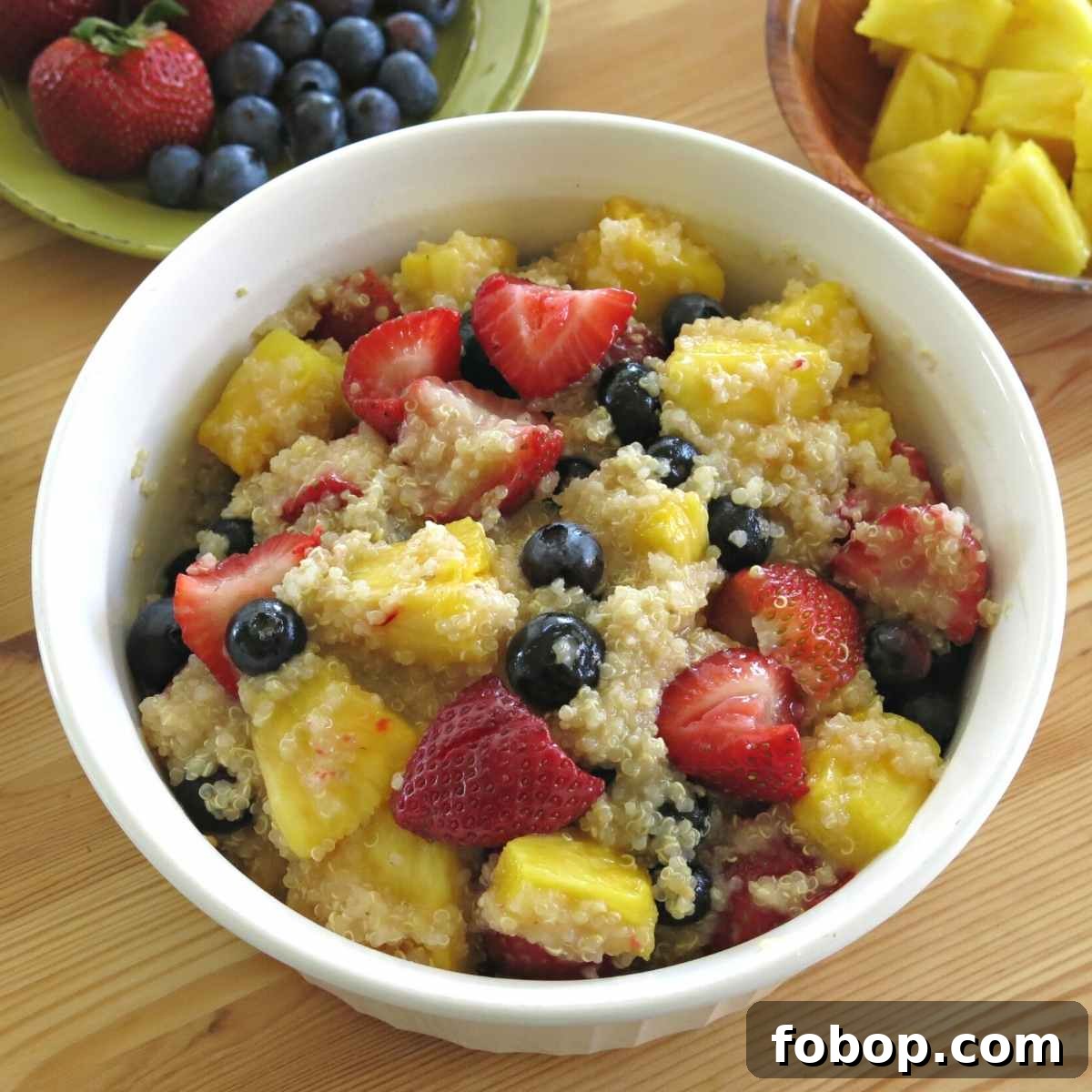 Quinoa fruit salad with honey lime dressing in a serving bowl with strawberries, blueberries, and pineapple next to it.