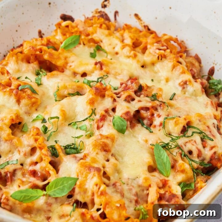 Melted cheese on top of pasta noodles mixed in a sauce in a white baking dish.