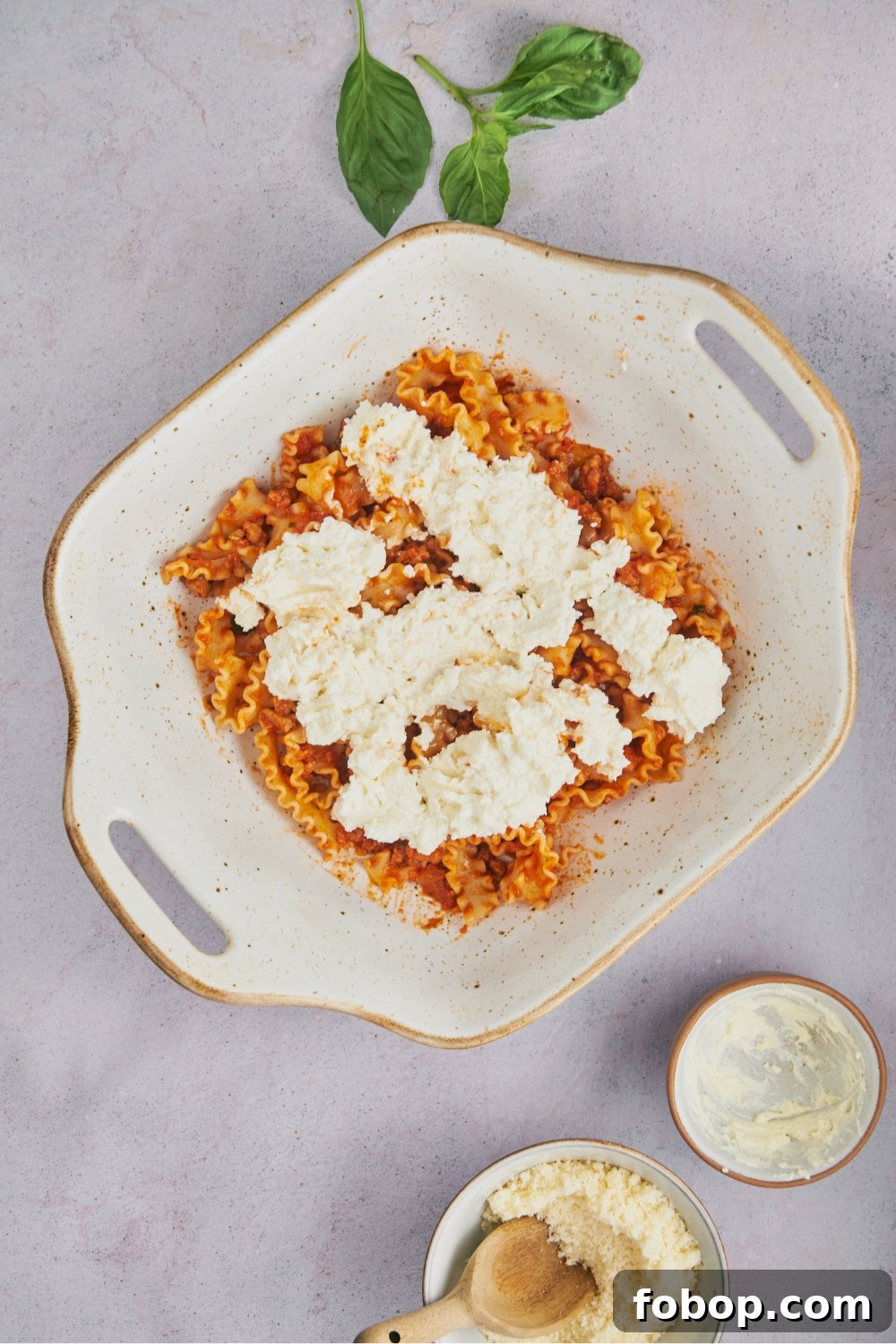 A casserole dish with pasta and red sauce and ricotta mix on top.