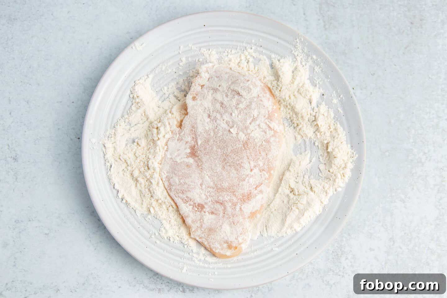 This is a picture of a chicken cutlet being dipped in flour.
