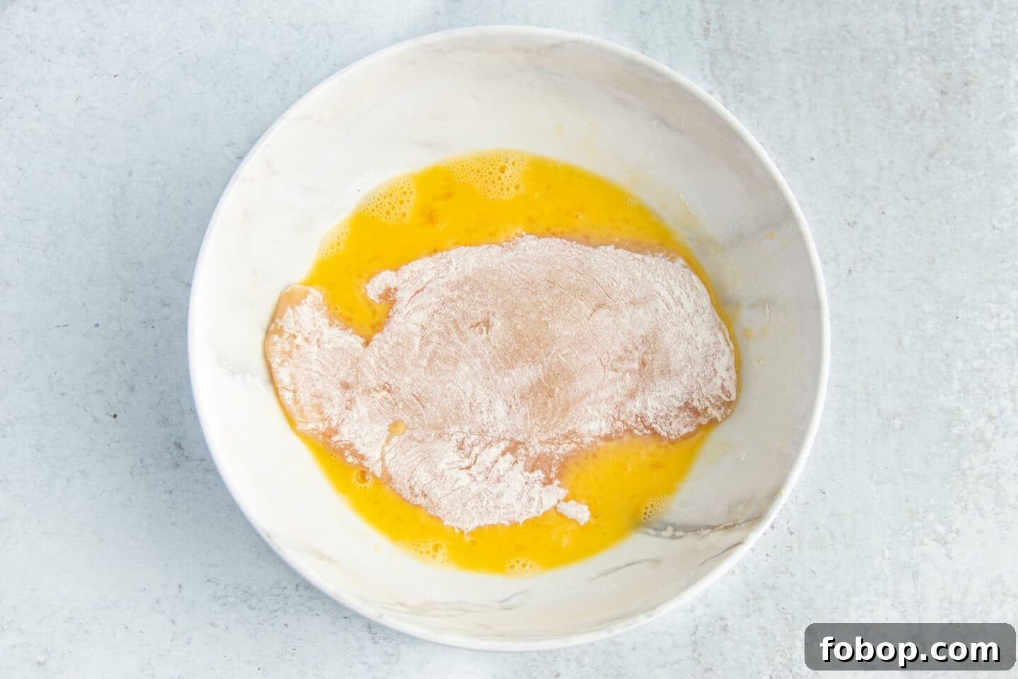 This is a picture of a chicken cutlet being dipped in egg wash.
