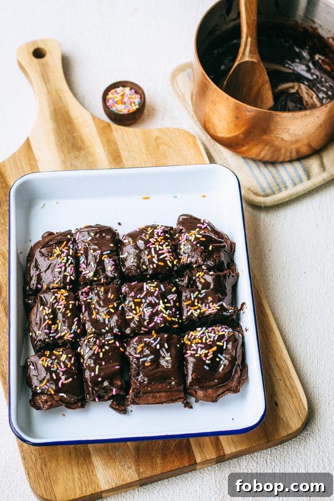 Gluten-Free Cosmic Brownies Recipe — Chewy Chocolate Treats 2 chocolate brownies with sprinkles on a white tray and wood cutting board with a pot of melted chocolate