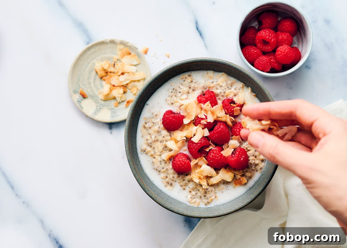Garnishing overnight oats with coconut milk, berries, and coconut flakes.