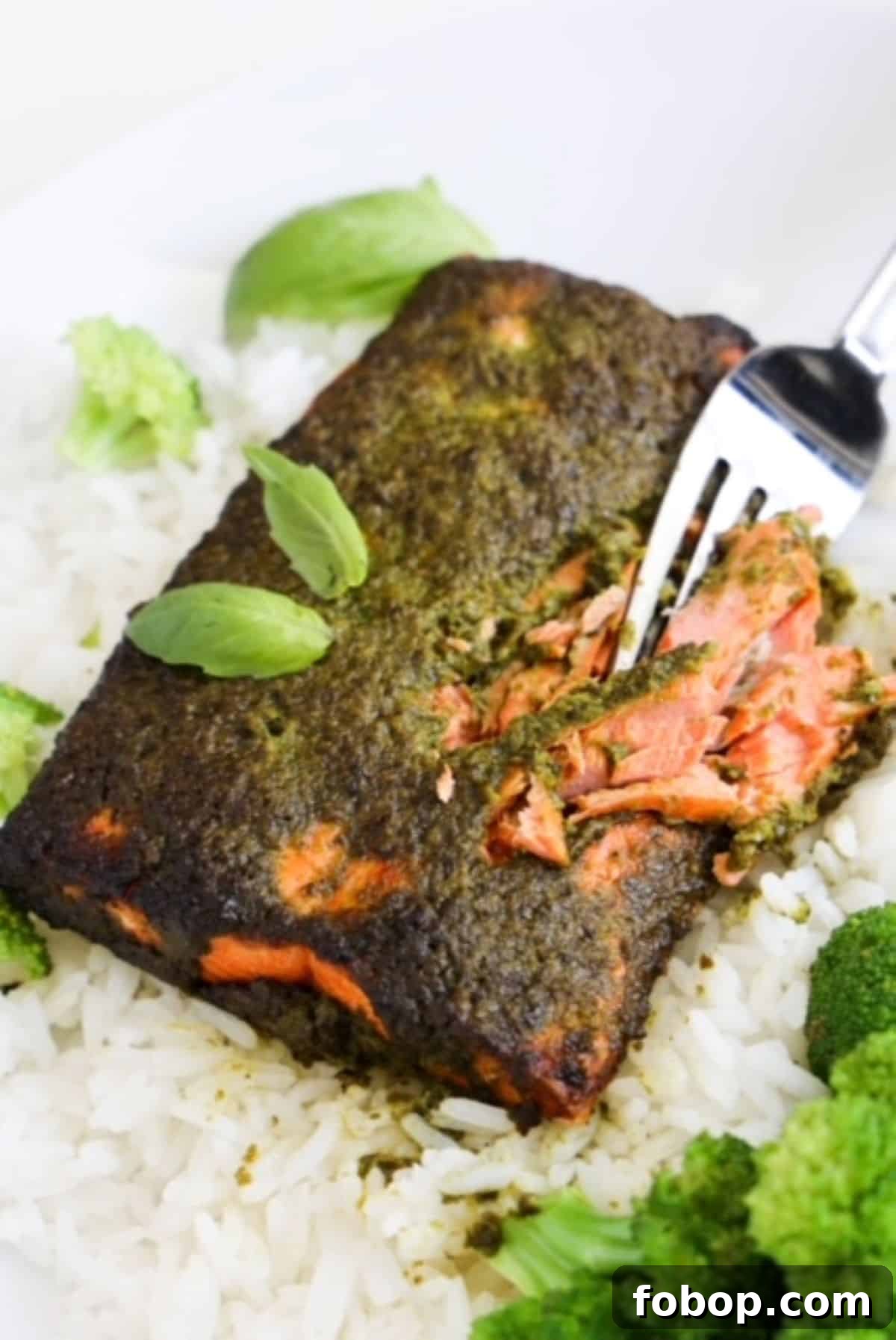 Crispy Air Fryer Frozen Salmon in 15 Minutes 2 A fork cutting into a piece of cooked salmon topped with pesto.