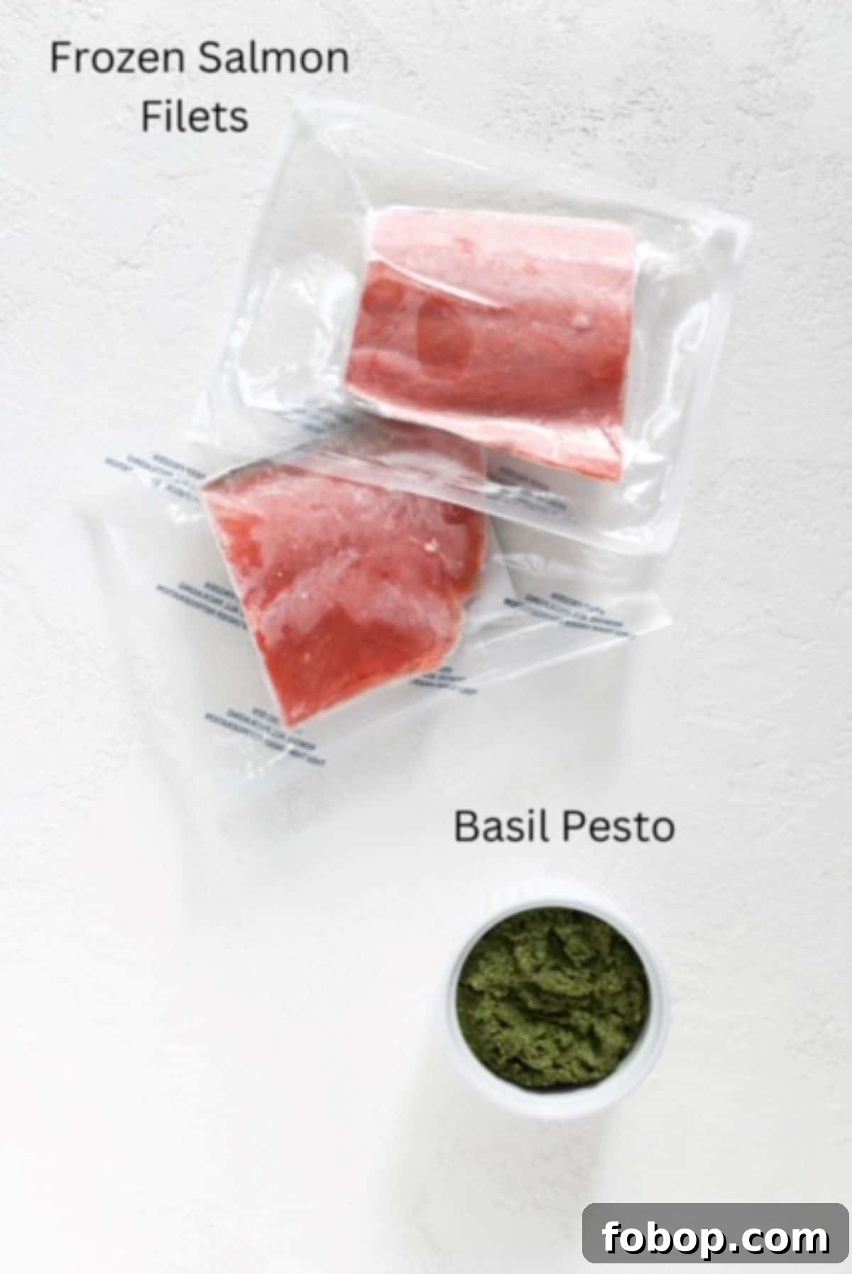 Crispy Air Fryer Frozen Salmon in 15 Minutes 3 Two pieces of frozen salmon vacuum sealed and pesto in a white serving dish, labeled.