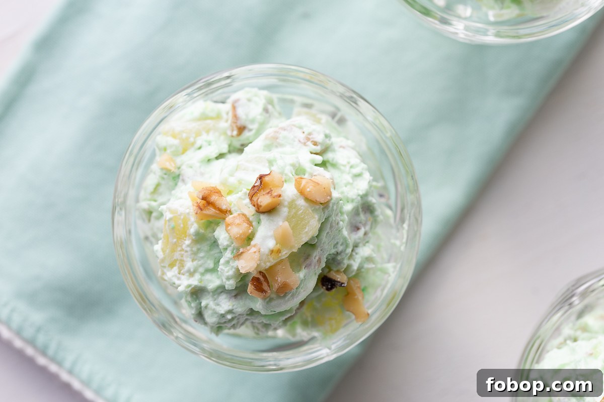 close up photo of pistachio pudding with walnuts in a glass dish, on a green cloth napkin