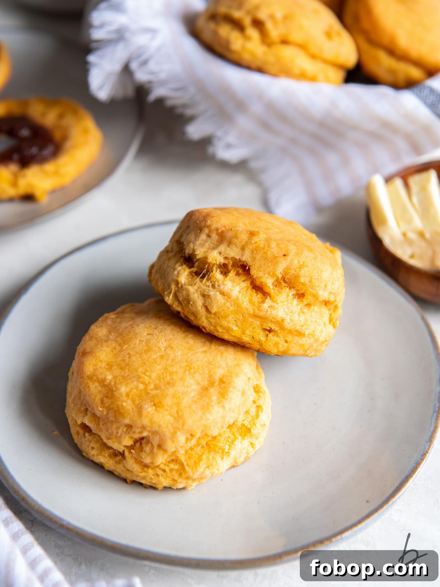 sweet potato biscuit leaning on another biscuit on a plate with small bowl of butter behind it.