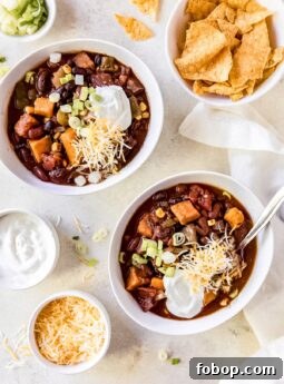 two bowls of sweet potato chili with sour cream, shredded cheese and green onion