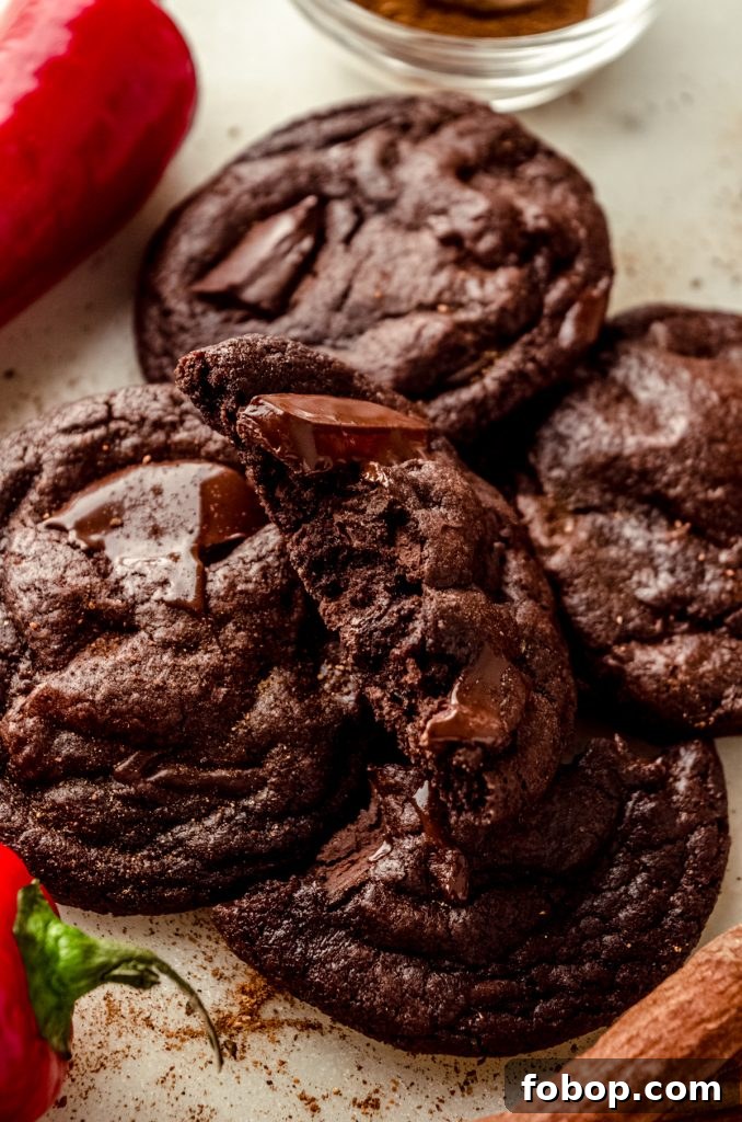 A chocolate cayenne cookie that has been split in half with a cinnamon stick, chili pepper, and nutmeg around it.