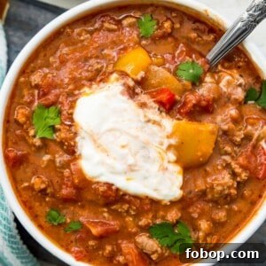 Ground Pork Chili Recipe Without Beans — Hearty Skillet Chili 14 A bowl of chili topped with sour cream with a spoon in it.