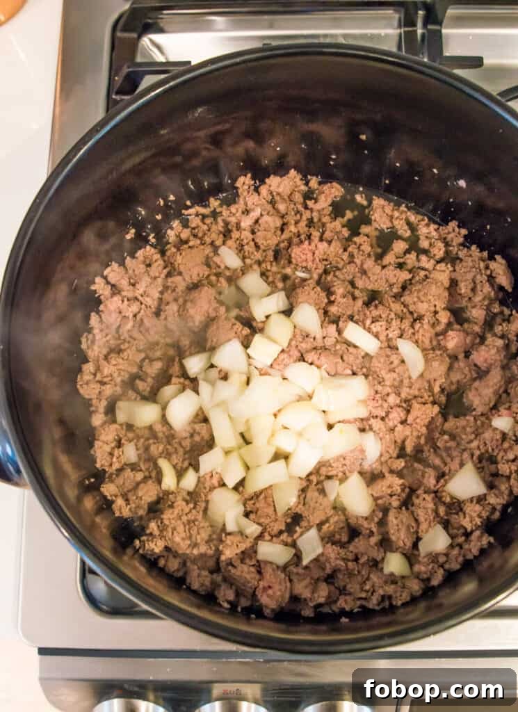 Ground Pork Chili Recipe Without Beans — Hearty Skillet Chili 6 A pot on the stovetop with cooked ground meat and chopped onion in it.
