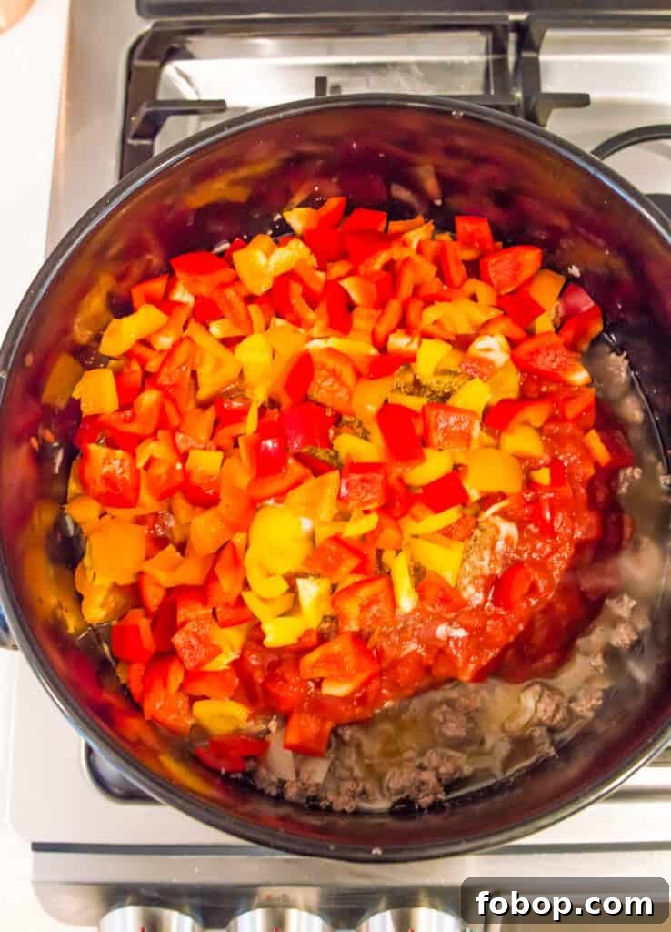 Ground Pork Chili Recipe Without Beans — Hearty Skillet Chili 7 A pot on the stovetop with cooked ground meat, tomatoes and chopped bell peppers in it.