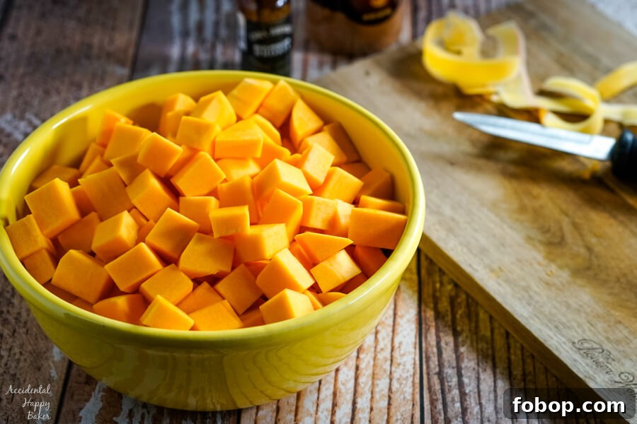 A yellow bowl of peeled and chopped butternut squash sits next to a cutting board and knife. 