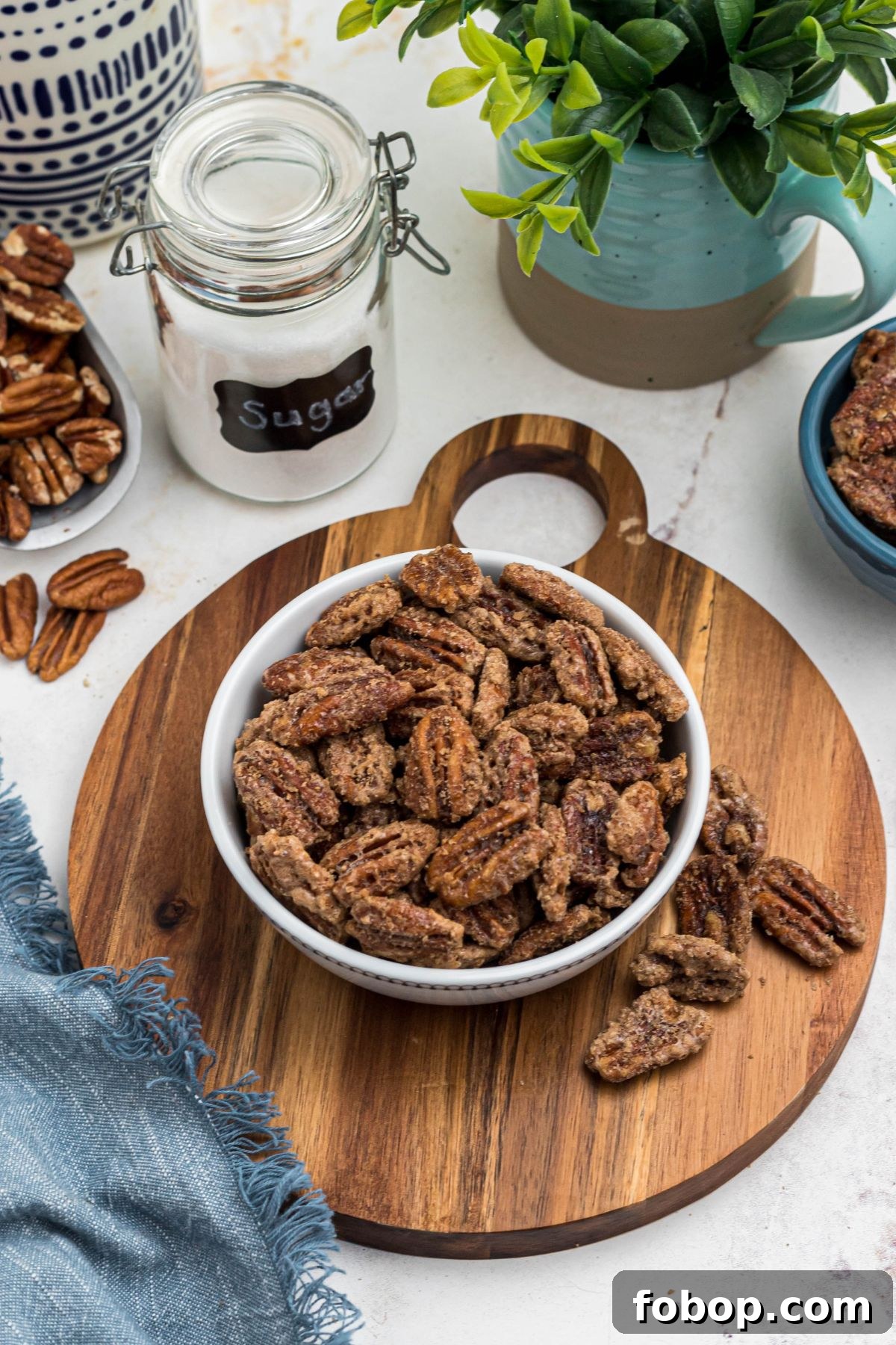 Sugar coated pecans in a white bowl with a small jar of sugar behind the bowl. 
