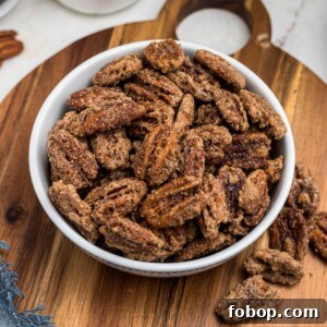 Sugar coated pecans in a white bowl with a small jar of sugar behind the bowl.