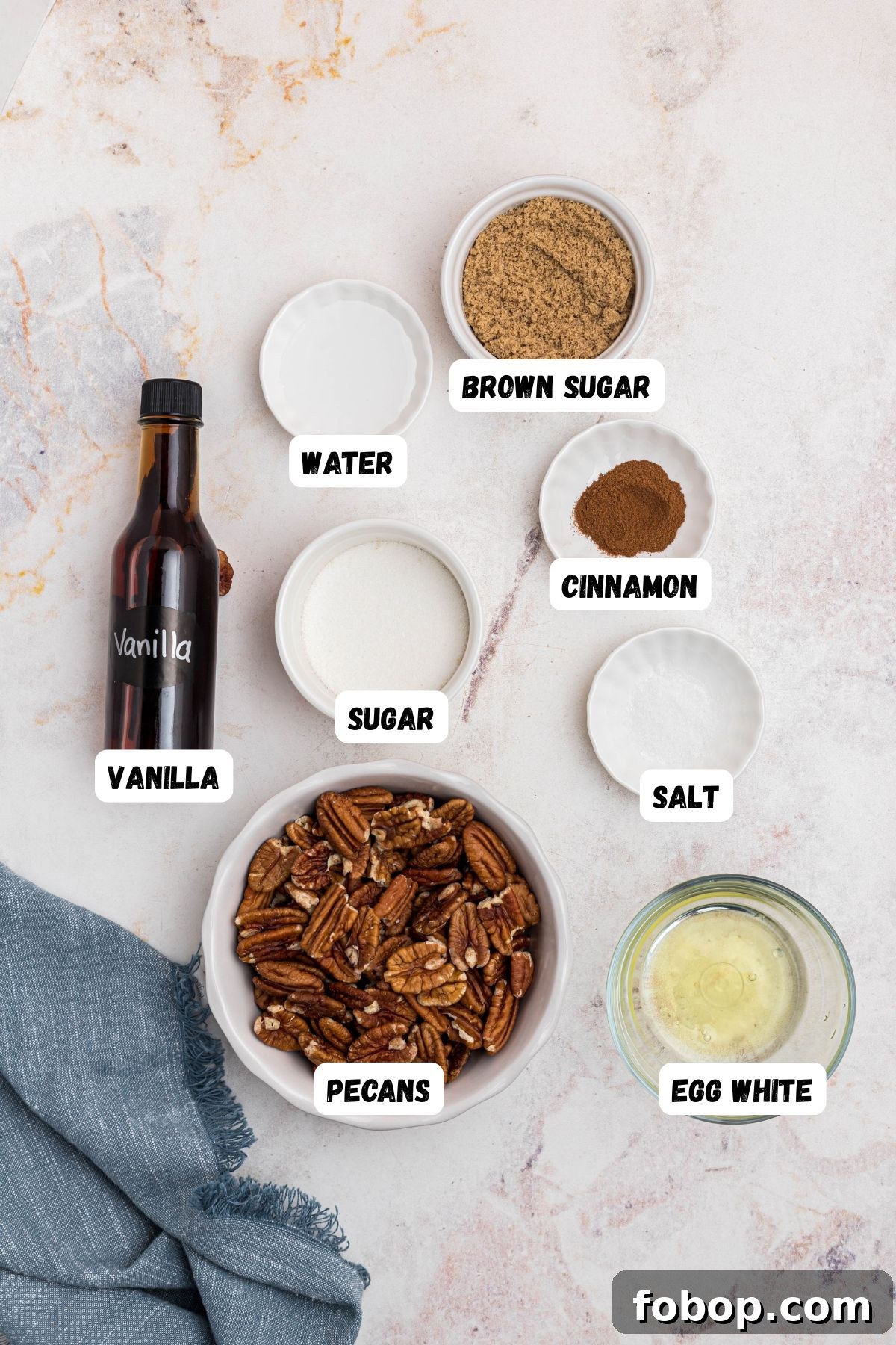 Ingredients needed to make candied pecans measured into small bowls and labeled on a marble table. 