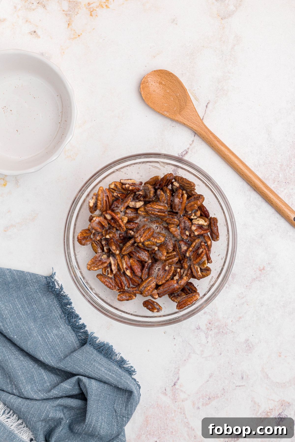 Pecans tossed together with whisked egg white in clear glass bowl. 