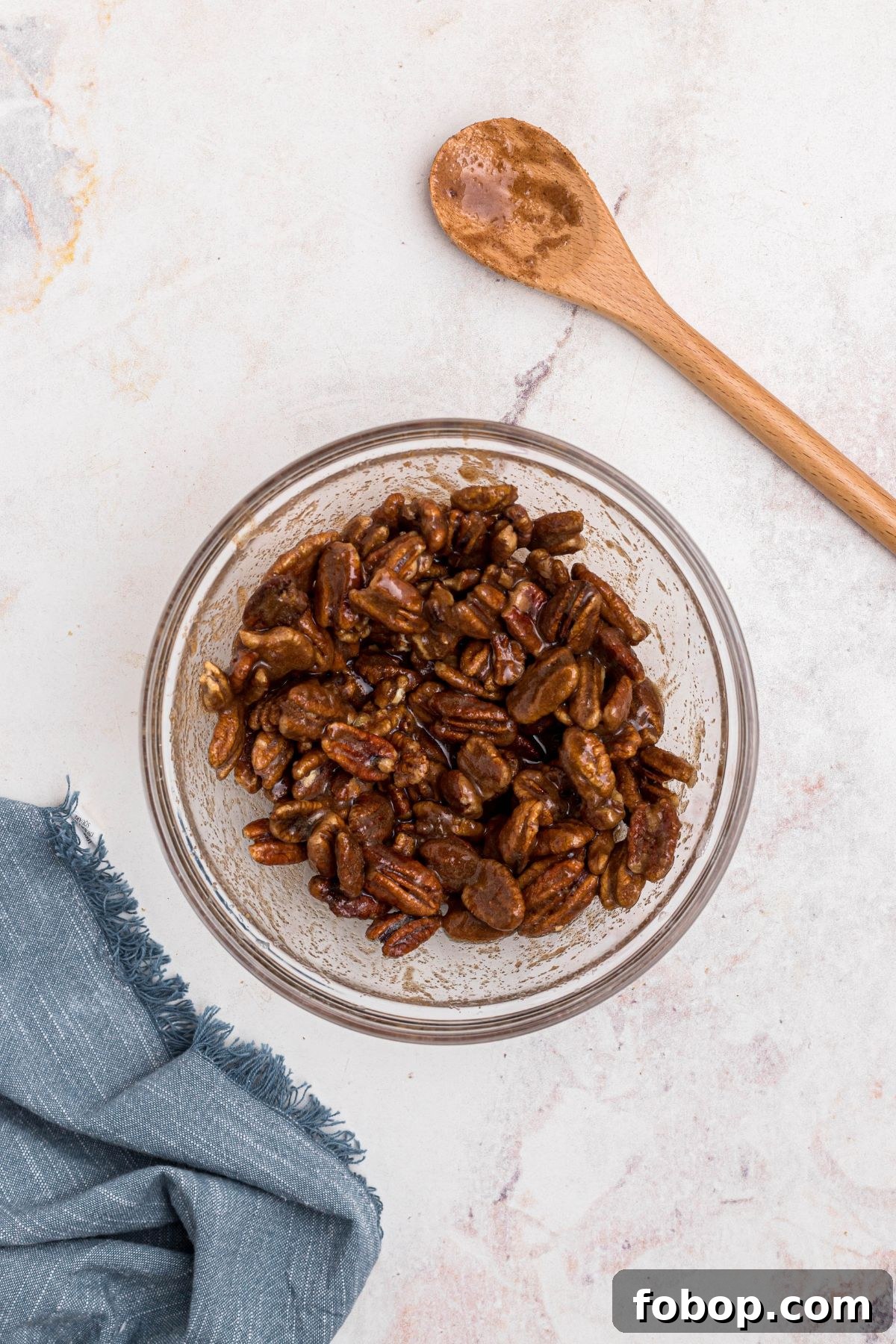 Sugars and cinnamon being tossed with coated pecans in a clear glass bowl on a marble table.