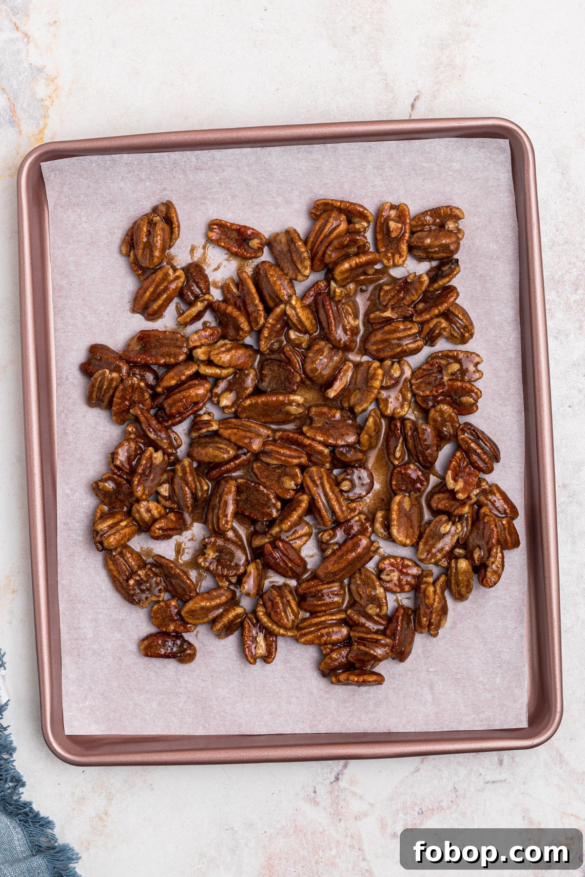 Coated pecans spread onto baking sheet, lined with parchment paper, before baking. 
