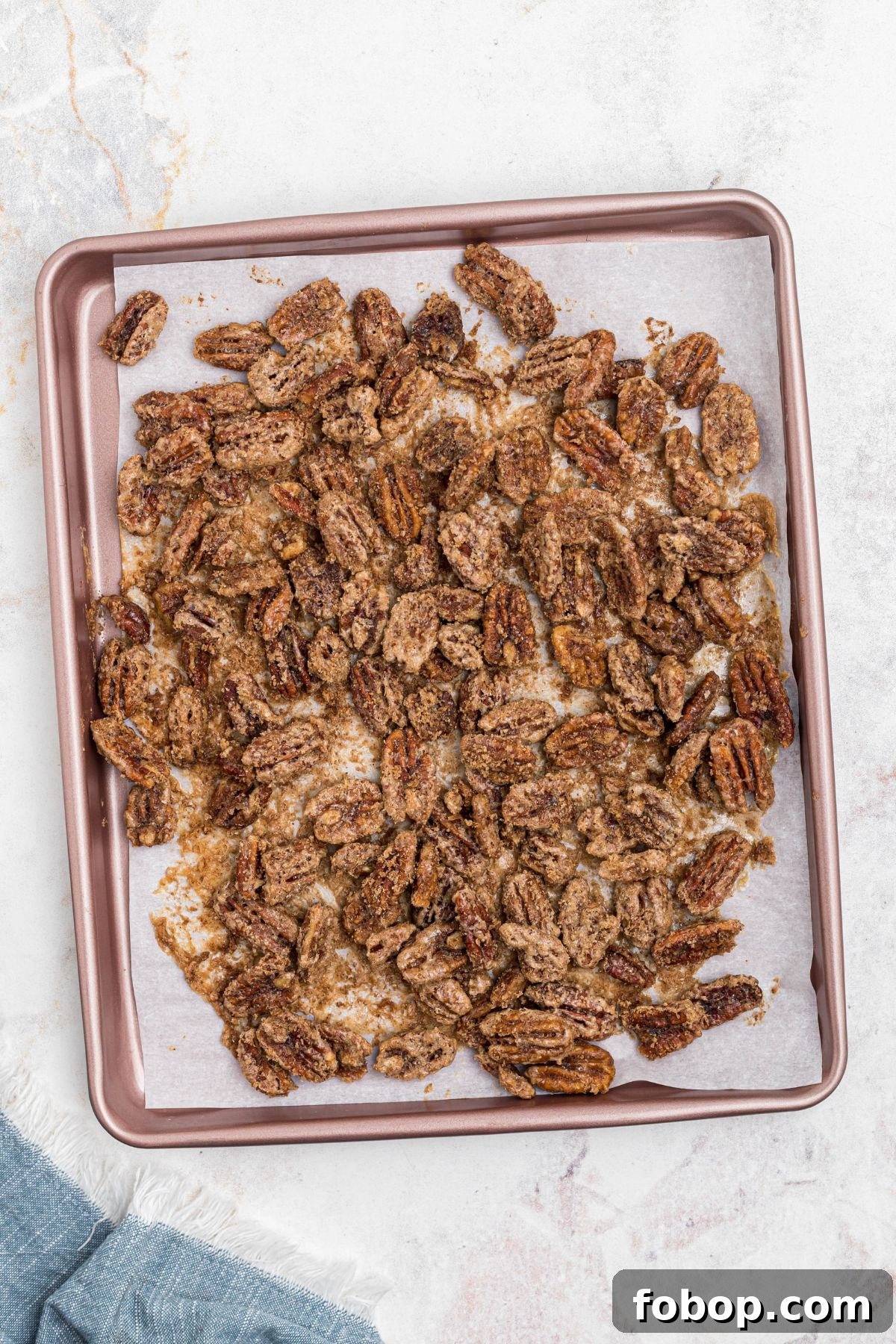 Pecans on baking sheet lined with parchment paper, coated with sugar, after baking. 