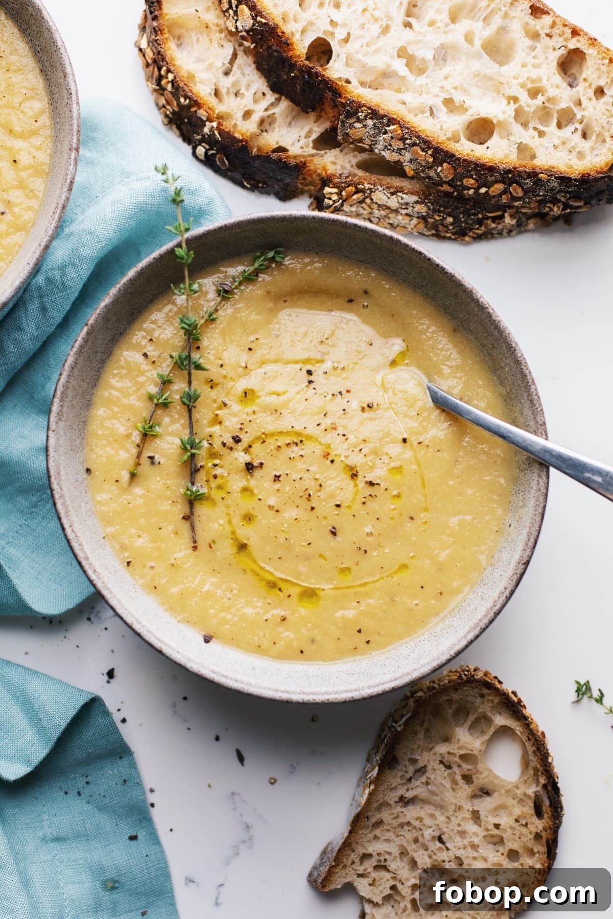 Creamy Vegan Cauliflower Soup Recipe — Dairy-Free Comfort Bowl 2 A grey bowl with cauliflower leek soup with a blue napkin and slices and bread next to it.