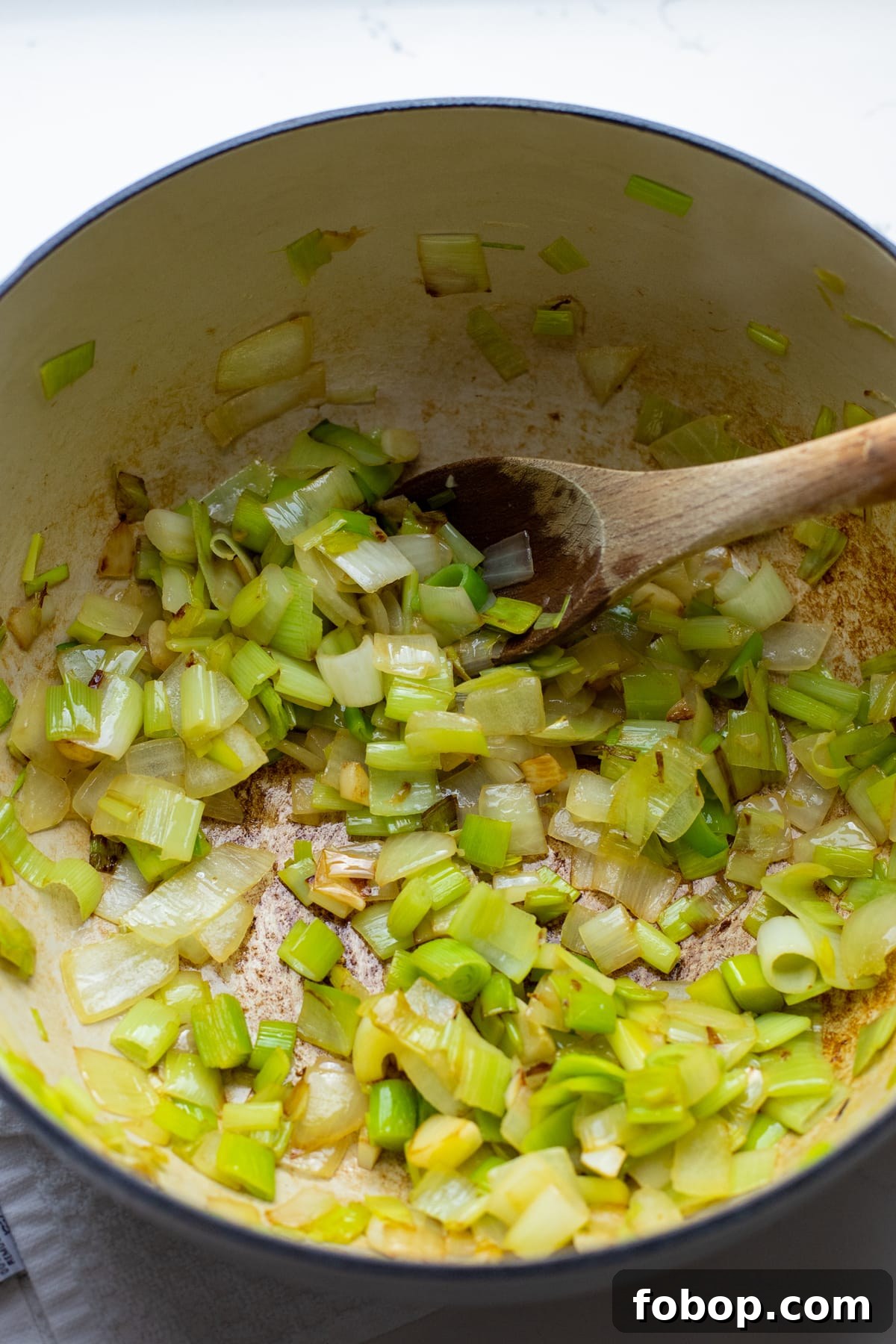 Creamy Vegan Cauliflower Soup Recipe — Dairy-Free Comfort Bowl 4 Sauteed leeks and onions in a white pot with a wooden spoon.