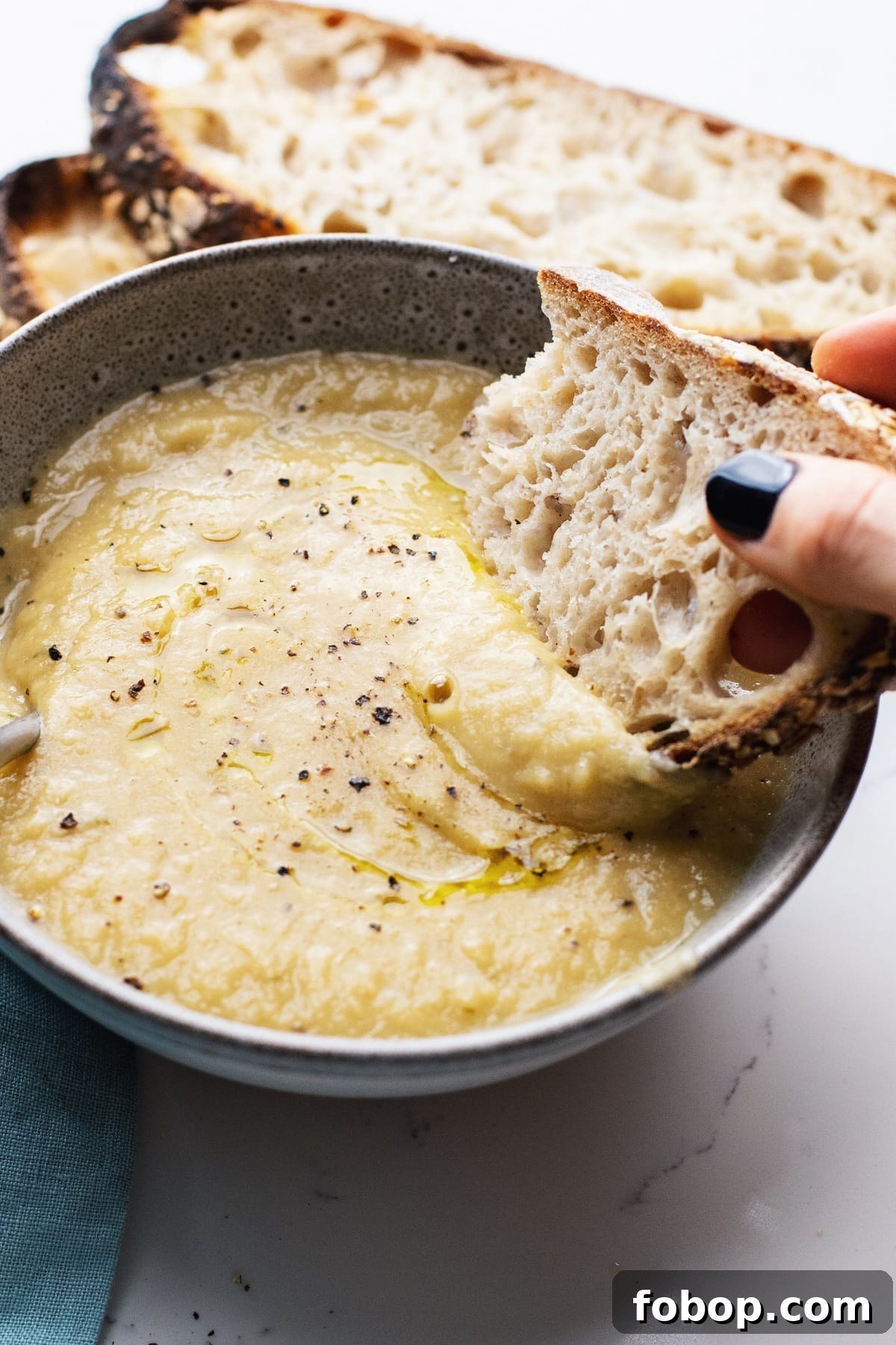 Creamy Vegan Cauliflower Soup Recipe — Dairy-Free Comfort Bowl 7 A hand dipping a piece of bread in a bowl of creamy cauliflower soup.
