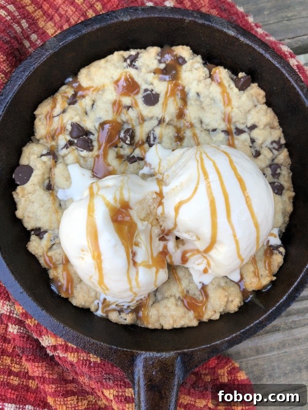 Overhead view of Chocolate Chip Skillet Cookie served with vanilla ice cream and caramel sauce in cast iron skillet from www.ApronFreeCooking.com