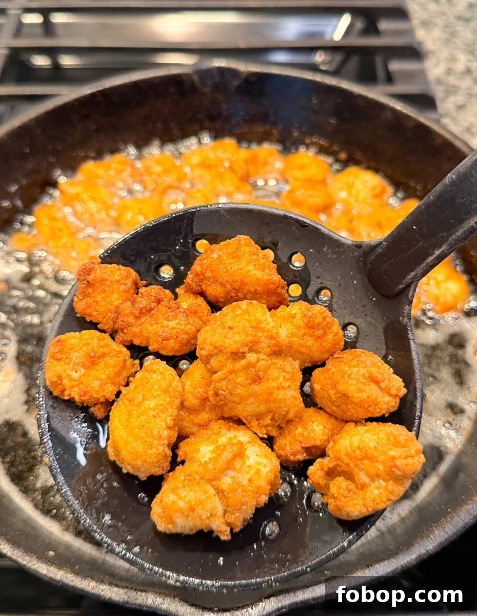 A slotted spoon lifting crispy fried chicken bites out of hot oil in a cast iron skillet.