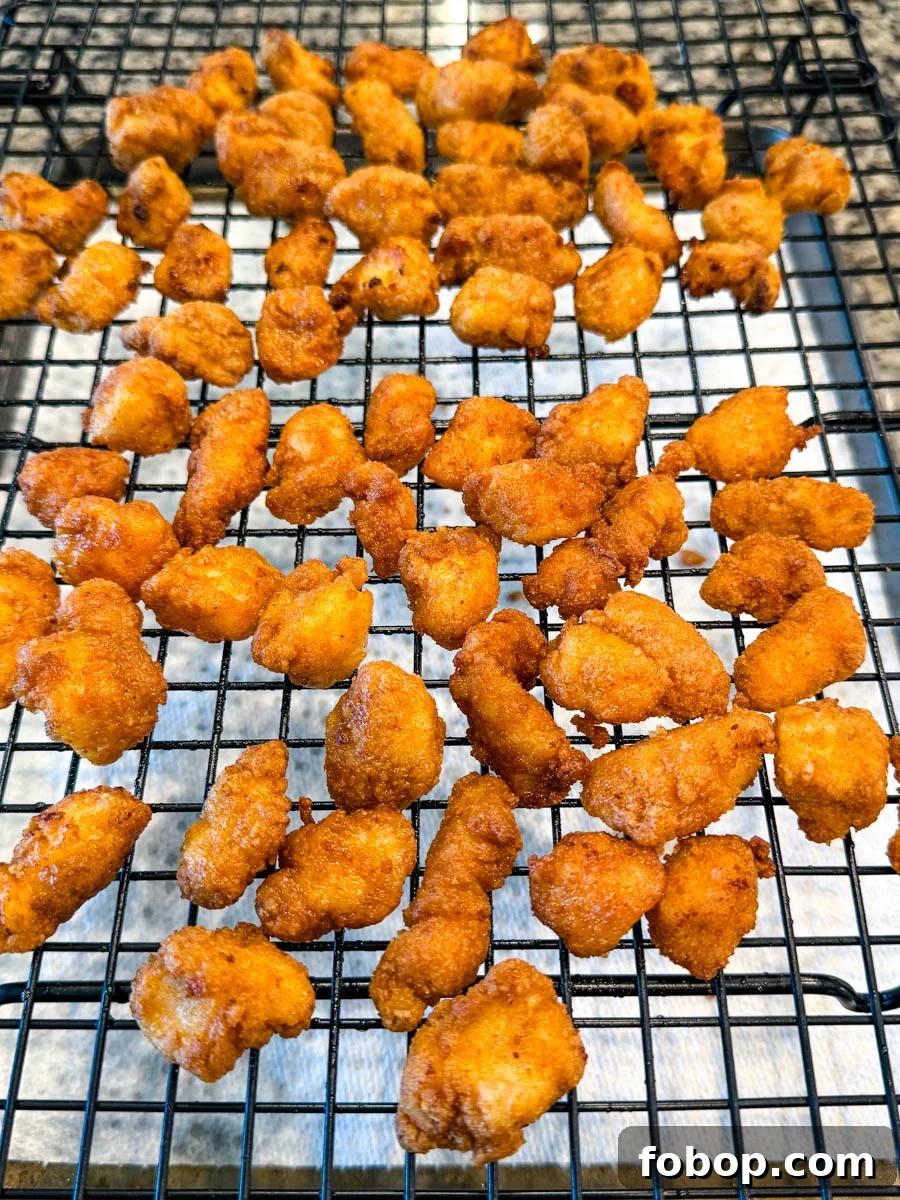 Golden brown fried chicken bites cooling on a wire rack over paper towels.